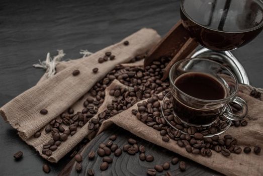 Coffee style, Cup of coffee and coffee beans roating with old wooden scoop and coffee beans around on the wooden and dark stone background. Oblique view from the top with copy space for your text.