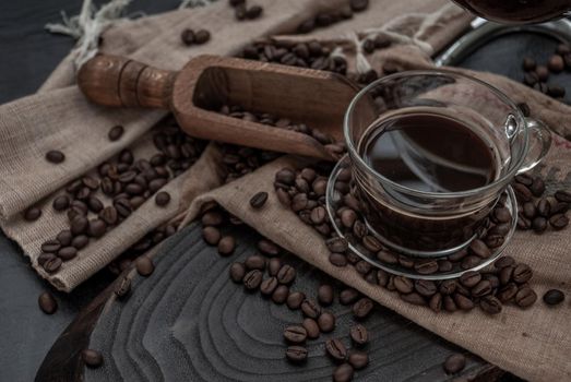 Coffee style, Cup of coffee and coffee beans roating with old wooden scoop and coffee beans around on the wooden and dark stone background. Close-up.
