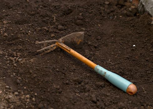 Iron hoe with plastic handle lies on black ground.
