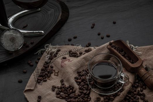 Coffee style, Cup of coffee and coffee beans roating with old wooden scoop and coffee beans around on the wooden and dark stone background. Oblique view from the top with copy space for your text.