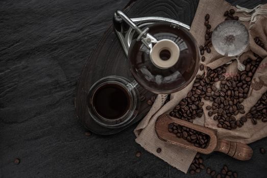Coffee style, Cup of coffee and coffee beans roating with old wooden scoop and coffee beans around on the wooden and dark stone background. Top view with copy space for your text.