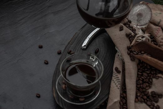 Coffee style, Cup of coffee and coffee beans roating with old wooden scoop and coffee beans around on the wooden and dark stone background. Oblique view from the top with copy space for your text.