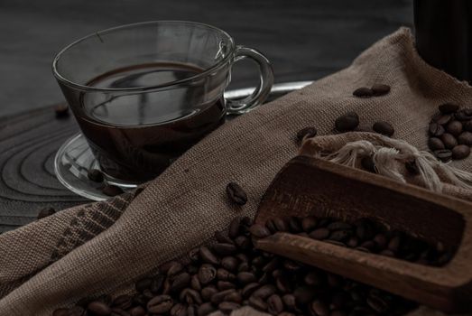 Coffee style, Cup of coffee and coffee beans roating with old wooden scoop and coffee beans around on the wooden and dark stone background. Close-up.