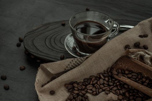 Coffee style, Cup of coffee and coffee beans roating with old wooden scoop and coffee beans around on the wooden and dark stone background. Oblique view from the top with copy space for your text.