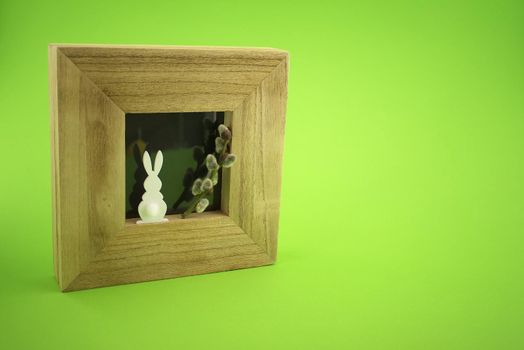 Easter Decoration with photo frame, Easter Rabbit figure and pussy willow branch over a green background. Happy Easter card concept with free copy space for text