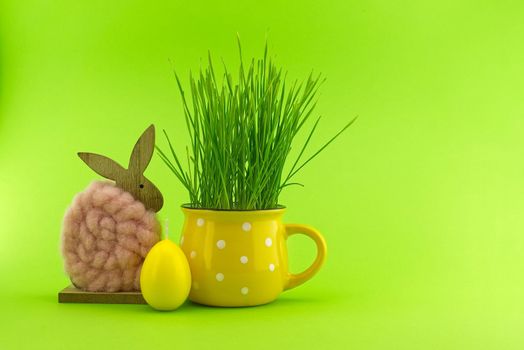 Easter Decoration with wheat seedlings growing from yellow cup, egg shaped candle and Easter Rabbit figure over a green background with free copy space for text