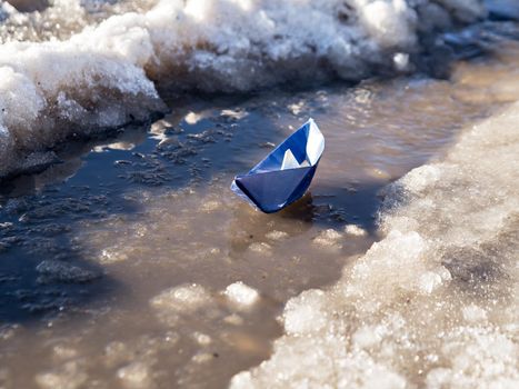 Paper boat floats on water amid melting snow.