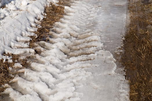 Tractor wheel tracks on melting snow and dark ground.