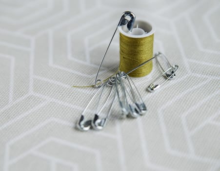 Tailor pins and spool of green thread on gray fabric.Selective focus