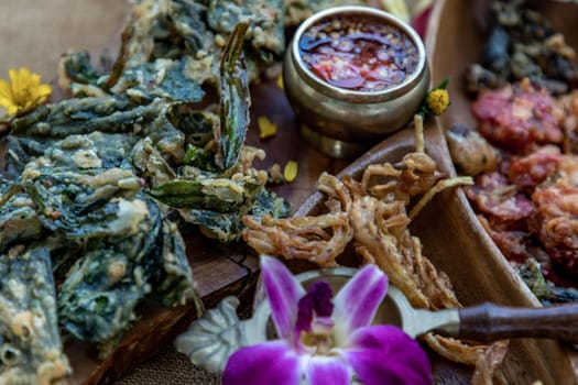 Close-up of Crispy Flowers, Crispy Herbs and Crispy Vegetables served  with Sweet sauce in a Wooden tray.
