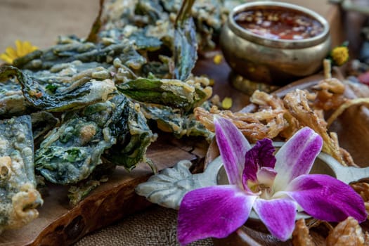 Close-up of Crispy Flowers, Crispy Herbs and Crispy Vegetables served  with Sweet sauce in a Wooden tray.