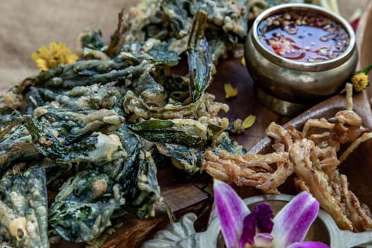 Close-up of Crispy Flowers, Crispy Herbs and Crispy Vegetables served  with Sweet sauce in a Wooden tray.