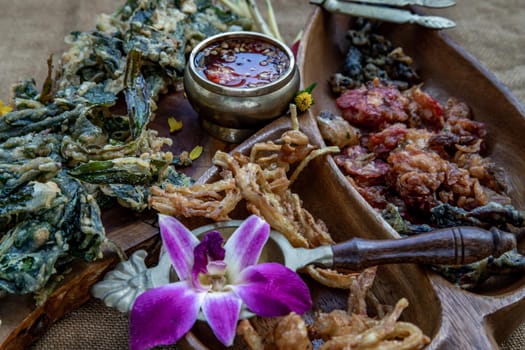 Close-up of Crispy Flowers, Crispy Herbs and Crispy Vegetables served  with Sweet sauce in a Wooden tray.