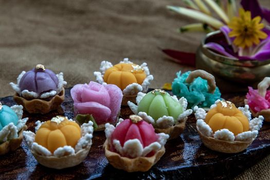 A variety of elegantly beautiful Thai Desserts (Khanom Wan Thai) colorful variations serving in a dark wooden, The bites in gold color and different flower shapes, Thai dessert, Auspicious dessert, Oblique view from the top.