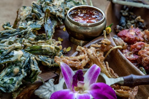 Close-up of Crispy Flowers, Crispy Herbs and Crispy Vegetables served  with Sweet sauce in a Wooden tray.