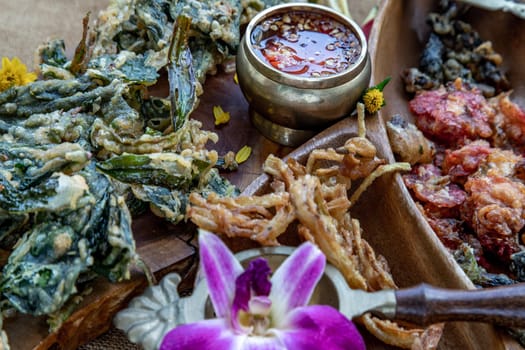 Close-up of Crispy Flowers, Crispy Herbs and Crispy Vegetables served  with Sweet sauce in a Wooden tray.