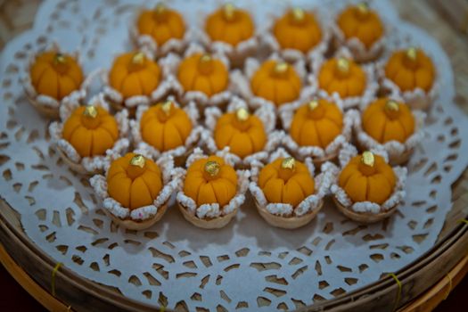 Elegantly beautiful Thai Desserts (Khanom Wan Thai) serving in a Bamboo basket hand made, The bites in gold color and different flower shapes.Thai dessert, Auspicious dessert, Selective focus.