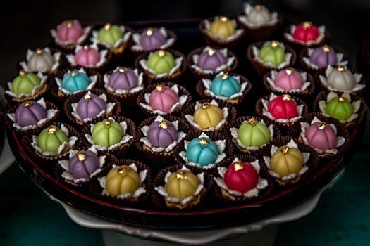 A variety of elegantly beautiful Thai Desserts (Khanom Wan Thai) colorful variations serving in a dark wooden, The bites in gold color and different flower shapes, Thai dessert, Auspicious dessert.