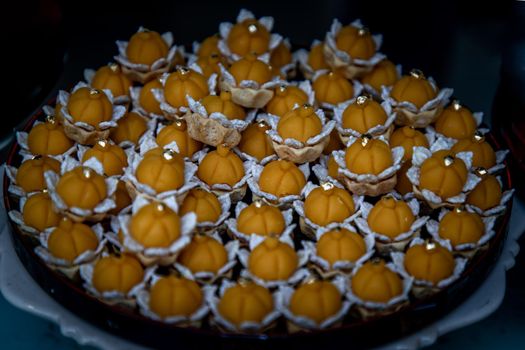 Elegantly beautiful Thai Desserts (Khanom Wan Thai) serving on a wooden background, The bites in gold color and different flower shapes.Thai dessert, Auspicious dessert.