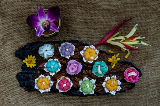 A variety of elegantly beautiful Thai Desserts (Khanom Wan Thai) colorful variations serving in a dark wooden, The bites in gold color and different flower shapes, Thai dessert, Auspicious dessert, Top view.
