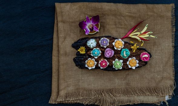 A variety of elegantly beautiful Thai Desserts (Khanom Wan Thai) colorful variations serving in a dark wooden, The bites in gold color and different flower shapes, Thai dessert, Auspicious dessert, Top view.