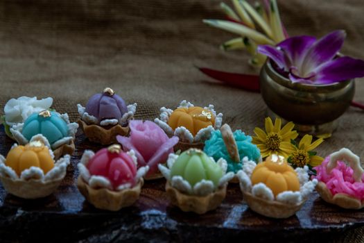 A variety of elegantly beautiful Thai Desserts (Khanom Wan Thai) colorful variations serving in a dark wooden, The bites in gold color and different flower shapes, Thai dessert, Auspicious dessert, Oblique view from the top.