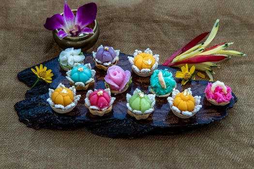 A variety of elegantly beautiful Thai Desserts (Khanom Wan Thai) colorful variations serving in a dark wooden, The bites in gold color and different flower shapes, Thai dessert, Auspicious dessert, Oblique view from the top.