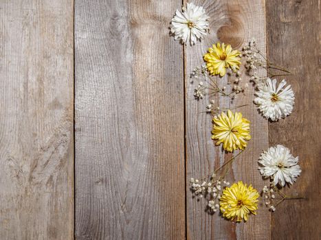 White and yellow flowers lie on wooden surface .