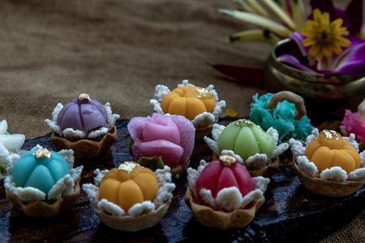 A variety of elegantly beautiful Thai Desserts (Khanom Wan Thai) colorful variations serving in a dark wooden, The bites in gold color and different flower shapes, Thai dessert, Auspicious dessert, Oblique view from the top.