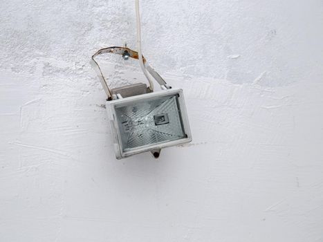 Lighting device in crumpled box with wire on white wall.