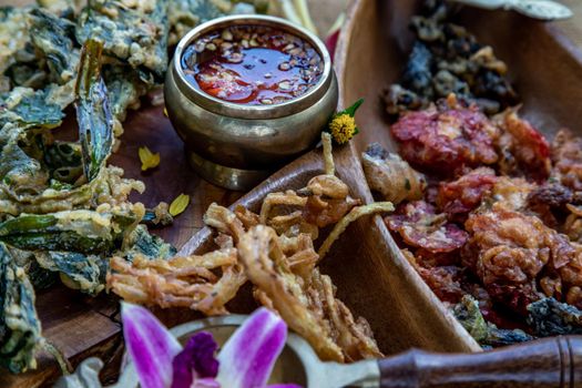 Close-up of Crispy Flowers, Crispy Herbs and Crispy Vegetables served  with Sweet sauce in a Wooden tray.