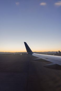 Astonishing view of clear dawn sky above planes parked in airport. Beautiful view of bright sunrise skyline from behind an airplane wing. Transportation and landscapes