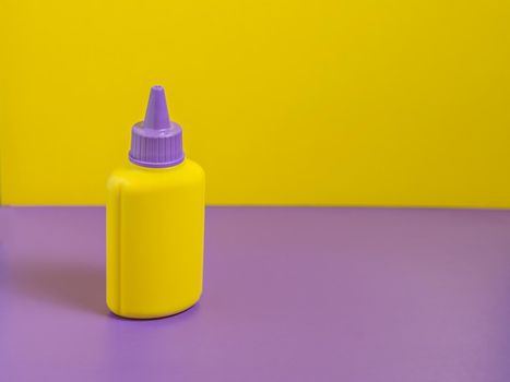 Yellow bottle with purple cap stands on purple table with yellow background.