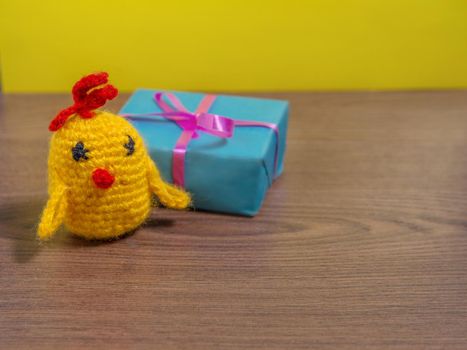 Toy yellow chicken next to gift in blue wrapper on brown table.