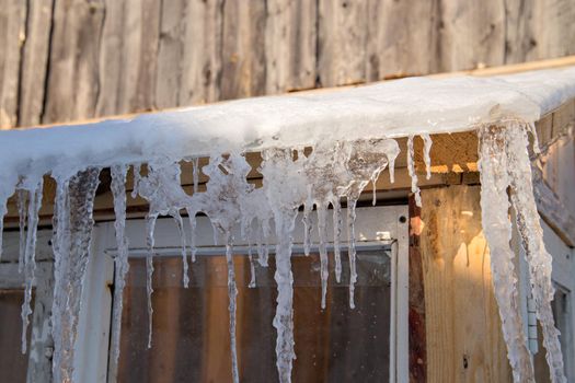 Spring ice icicles on roof of greenhouse. Patterns scattered by sun and frost. Selective focus