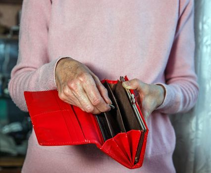 Elderly woman pulls out last coins from red purse.
