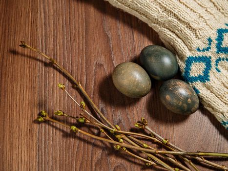 Painted eggs, willow twigs with green kidneys lie on brown surface of rows with knitted jacket.