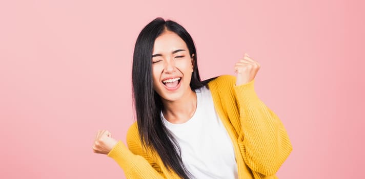 Happy Asian portrait beautiful cute young woman standing winning and surprised excited screaming open mouth raise hands, studio shot isolated pink background, Thai female wow with copy space