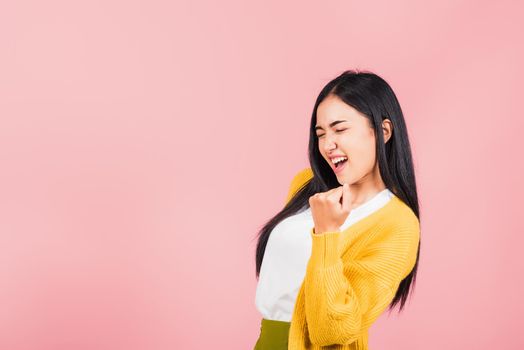 Happy Asian portrait beautiful cute young woman stand makes raised fists up celebrating her winning success gesture, studio shot isolated pink background, Thai female excited say yes! with copy space