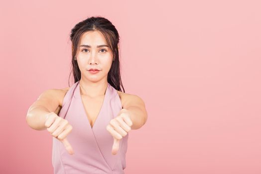 Portrait Asian beautiful young woman unhappy, negative gesture showing finger thumbs down or dislike sign, studio shot isolated on pink background, Thai female rejection unlike with copy space