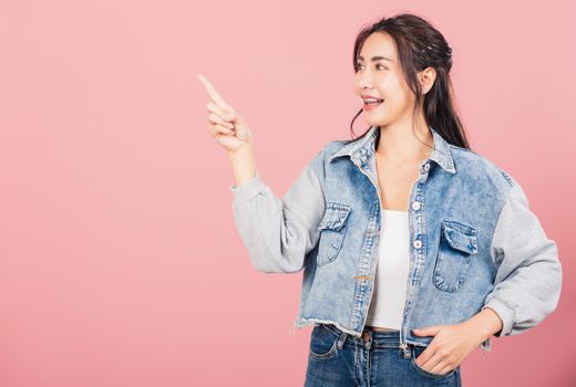 Happy Asian portrait beautiful cute young woman standing smiling indicate finger empty space looking to camera, studio shot isolated on pink background, Thai female pointing index out with copy space