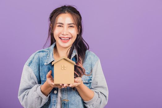 Happy Asian portrait beautiful cute young woman wear denim excited smiling holding house model on hand, studio shot isolated on purple background, broker female hold home real estate insurance