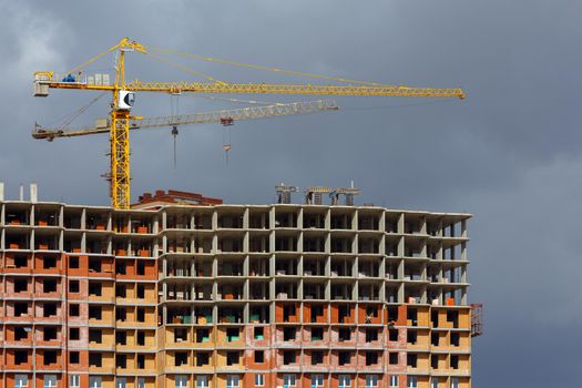building process of large residential apartment building with crane on cloudy sky background.