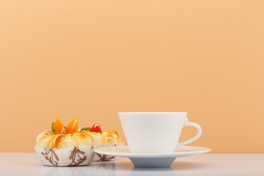 White ceramic tea or coffee cup with sweets next to it against beige background with copy space. High quality photo