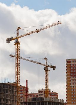 building process of large residential apartment building with crane on cloudy sky background.