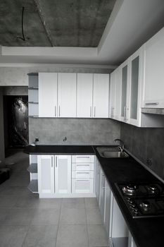 Modern minimalism style kitchen interior in monochrome tones. Custom kitchen with grey white facadesmdf and dark grey countertop with installed kitchen hood and sink. Modular kitchen from chipboard