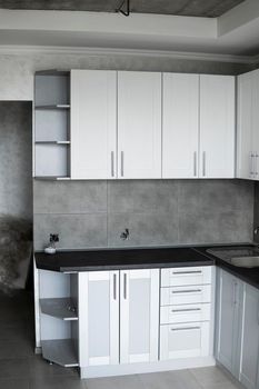 Modern minimalism style kitchen interior in monochrome tones. Custom kitchen with grey white facadesmdf and dark grey countertop with installed kitchen hood and sink. Modular kitchen from chipboard