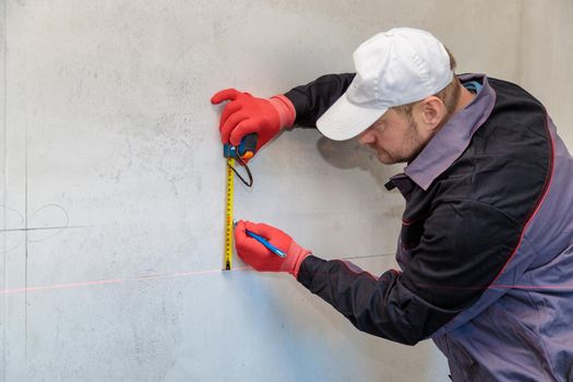 A man, an electrician marks out with a pencil, tape measure and a linear level for drilling holes for sockets