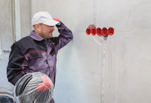 An electrician stands against the wall with an electrical cable for sockets. Close-up