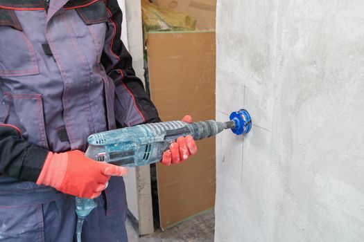 An electrician drills holes for sockets with a diamond core bit. Close-up